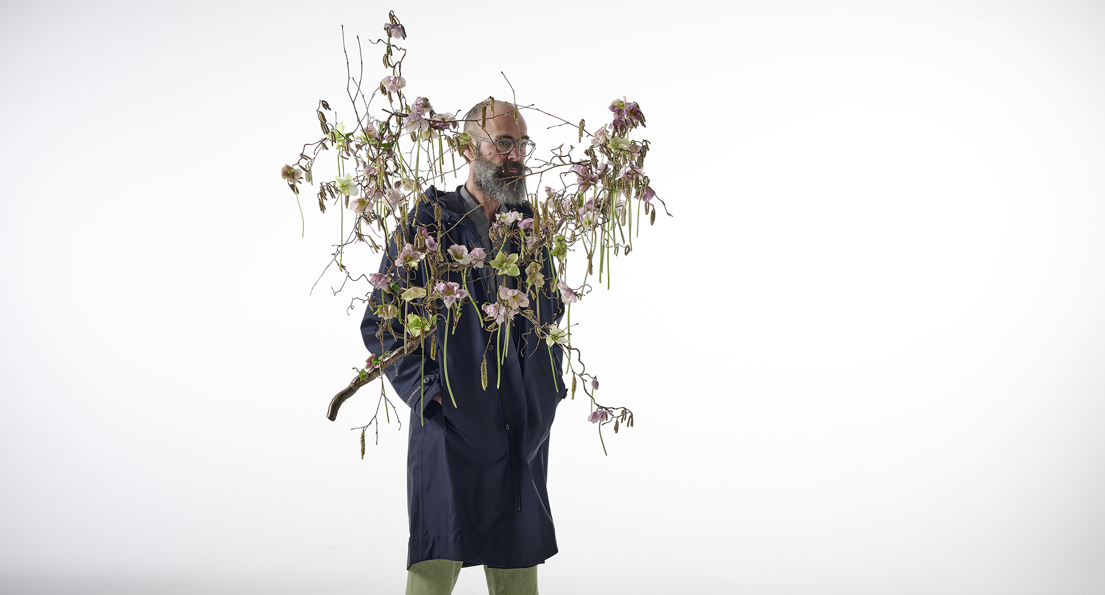 Mann stehend mit Regenjacke hinter einem floralen Objekt