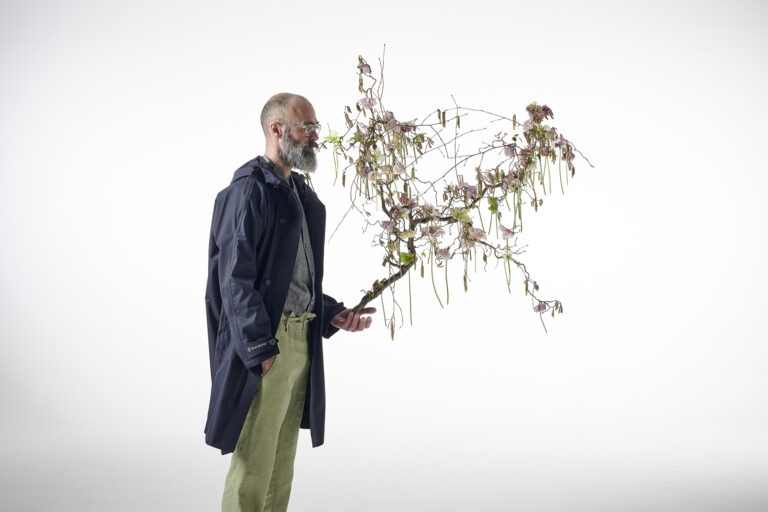 Mann stehend mit Regenjacke und Floralem Objekt